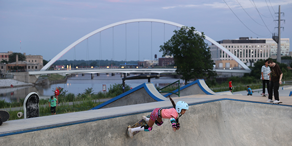 A young girl  skateboarding with a Des Moines bridge in the background