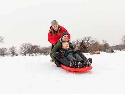 A woman pushing man and child on a sled down a hill.